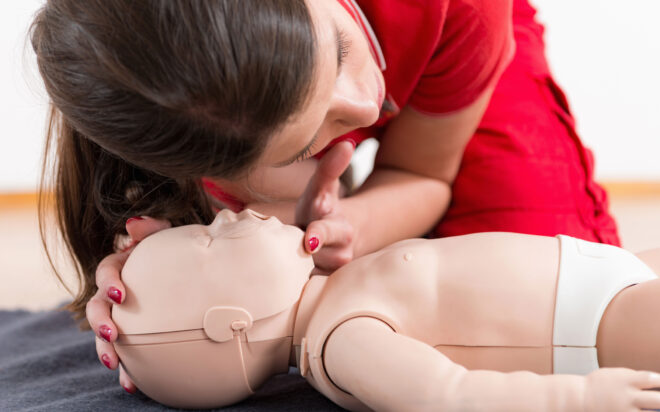 Woman checking breathing of an infant-sized CPR training dummy