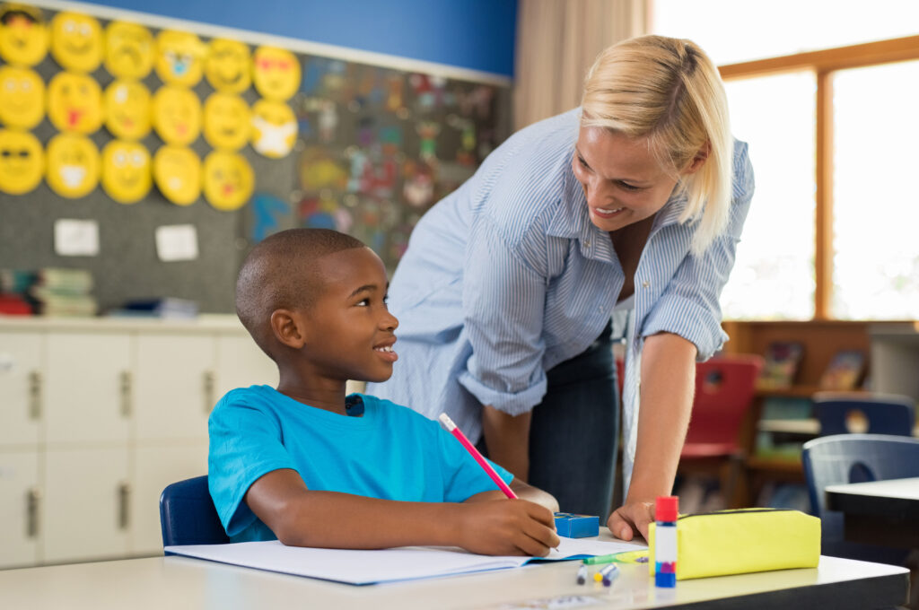 Paraprofessional or teacher helping an elementary-school aged child in a classroom.