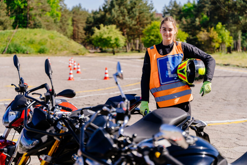 Woman holding a motorcycle helmet while standing next to motorcycles on a training course