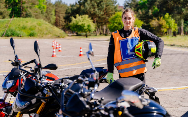 Woman holding a motorcycle helmet while standing next to motorcycles on a training course