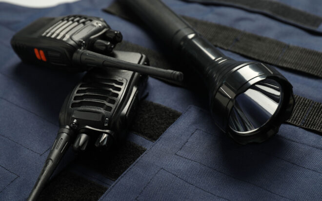 Closeup of two walkie talkies and a flashlight on a dark blue law enforcement tactical jacket.