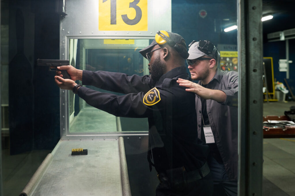 A firearms instructor helps a security guard line up a shot with a handgun in an indoor firearms training range.