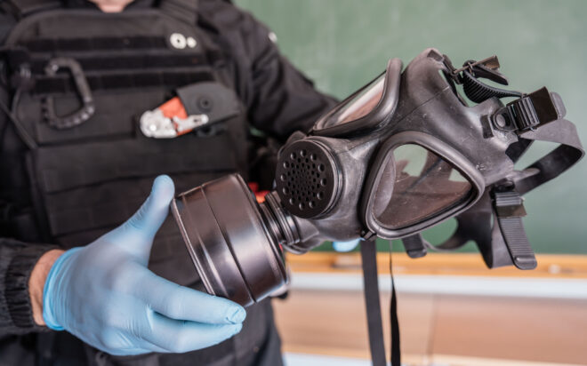 Closeup of law enforcement officer wearing blue nitrile gloves holds up a modern gas mask.